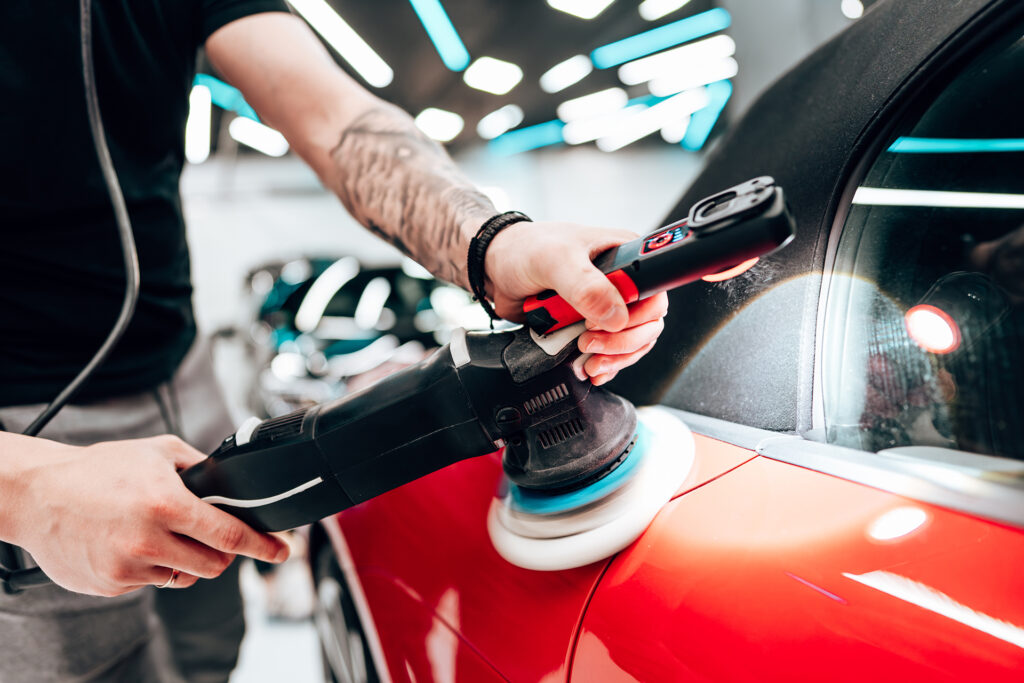 Professional car detailer using an orbital polisher to polish the hood of a red car