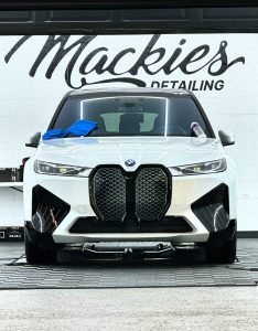 Front view of a white BMW inside Mackie’s Detailing studio with microfiber towels and detailing products on the hood, highlighting professional paint correction and ceramic coating services.